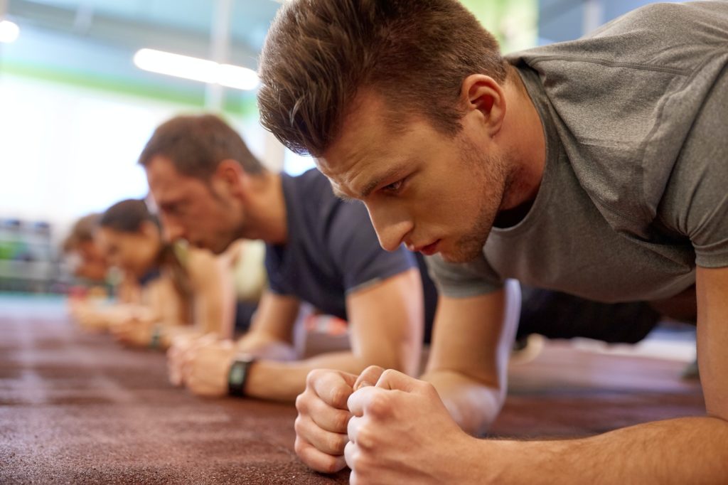 man doing plank exercise at group training in gym